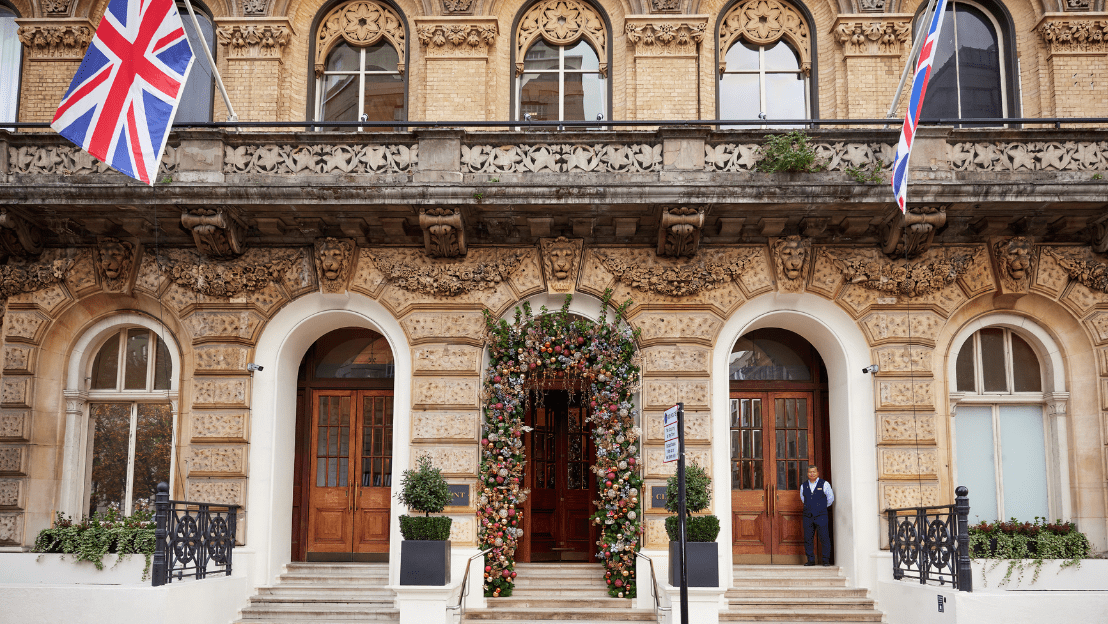 Historic hotel façade with arched windows, Union Jack flags, and a floral arch framing the main entrance, with steps leading up from the street.