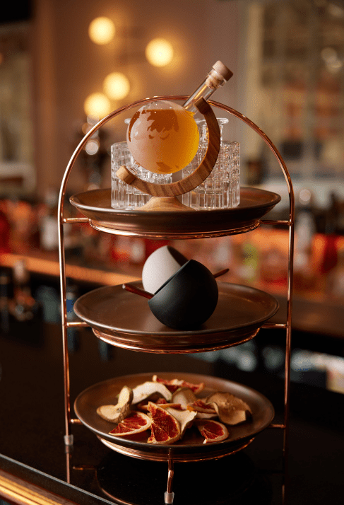 Three-tiered stand with drinks, bowls, and dried citrus on a bar counter