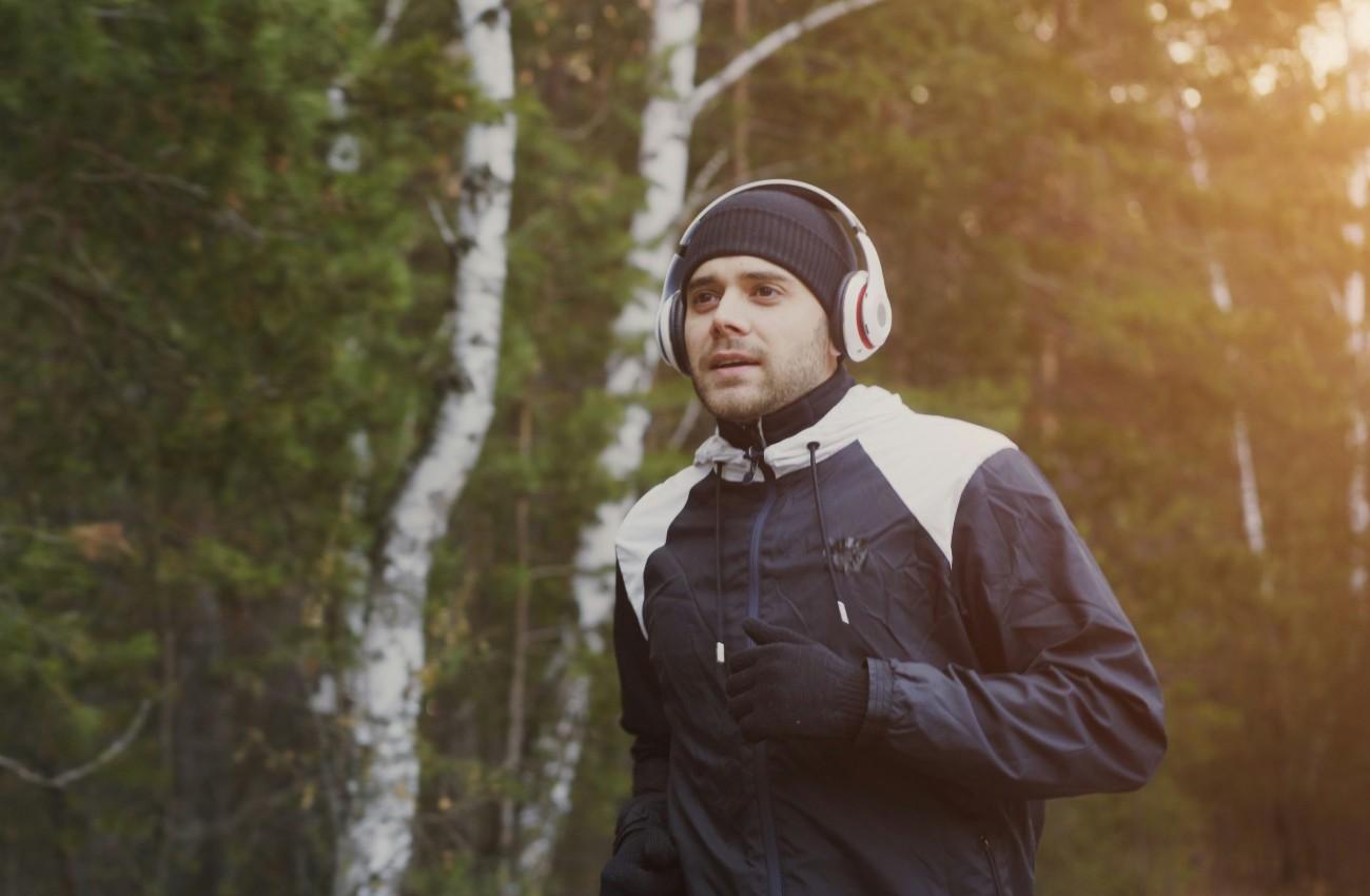 Man wearing headphones and sportswear running through a park in low sunlight.