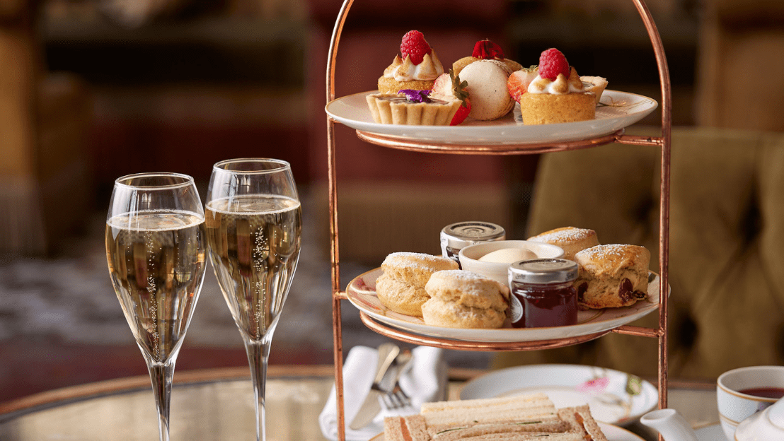 Afternoon tea setup with pastries, scones, champagne, and finger sandwiches in an elegant setting