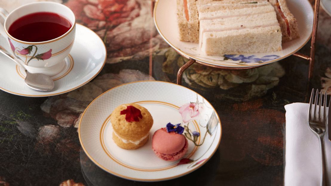 Tea setting with floral china, finger sandwiches, and pastries on a table