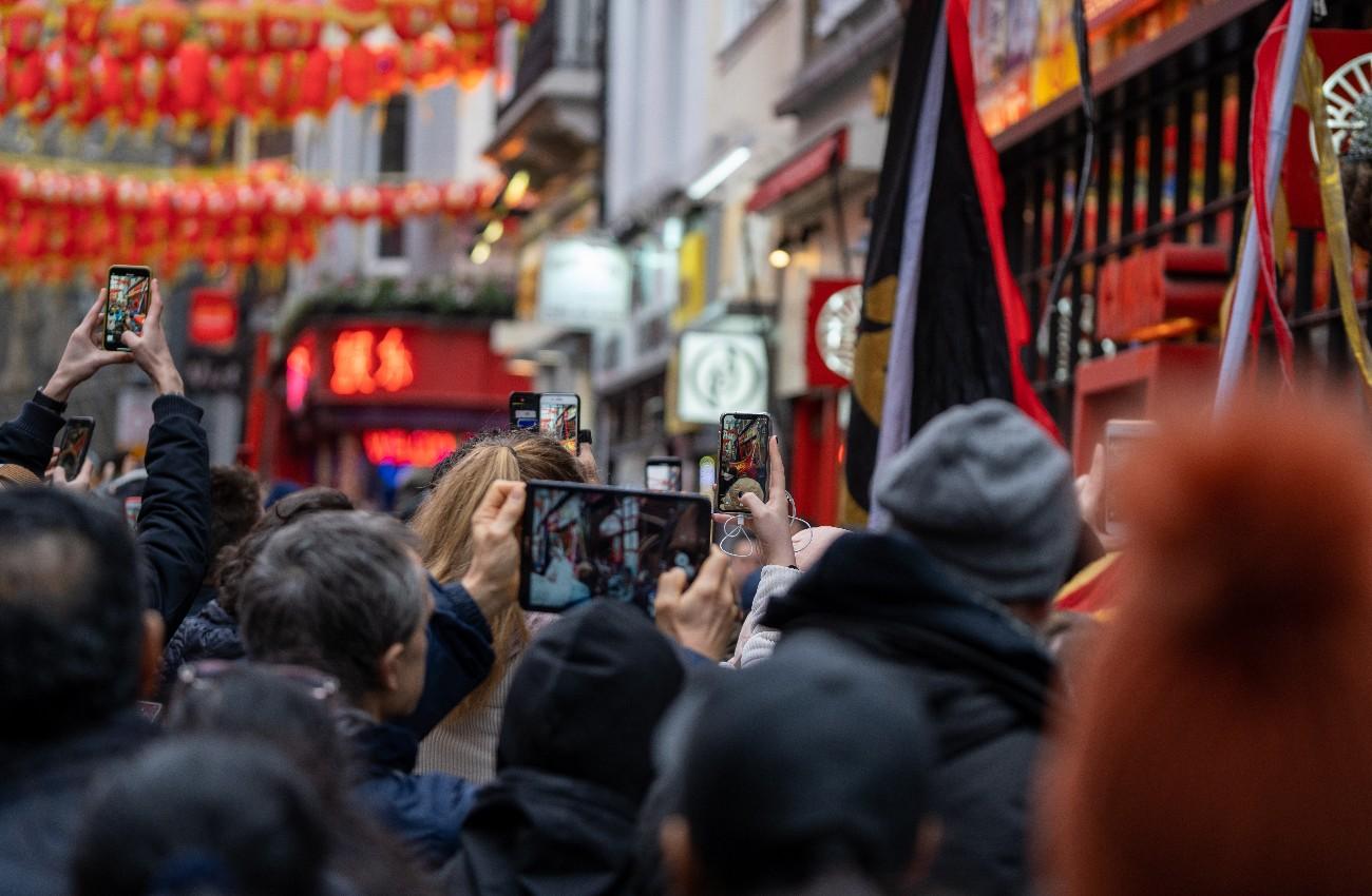 Crowd photographing red lanterns and decorations on a busy Chinatown street.