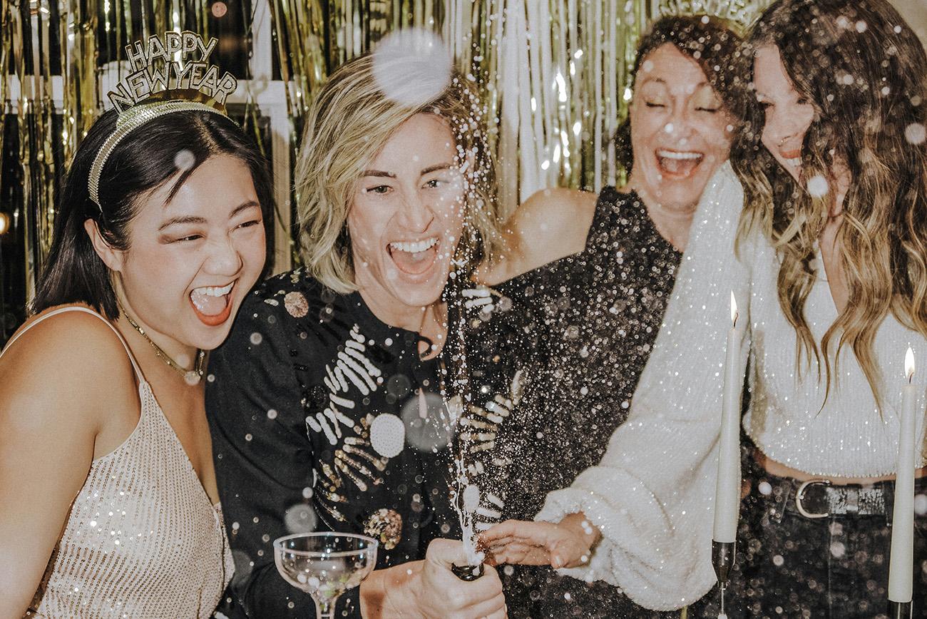 Group of four women celebrating new year's eve with Champagne popping