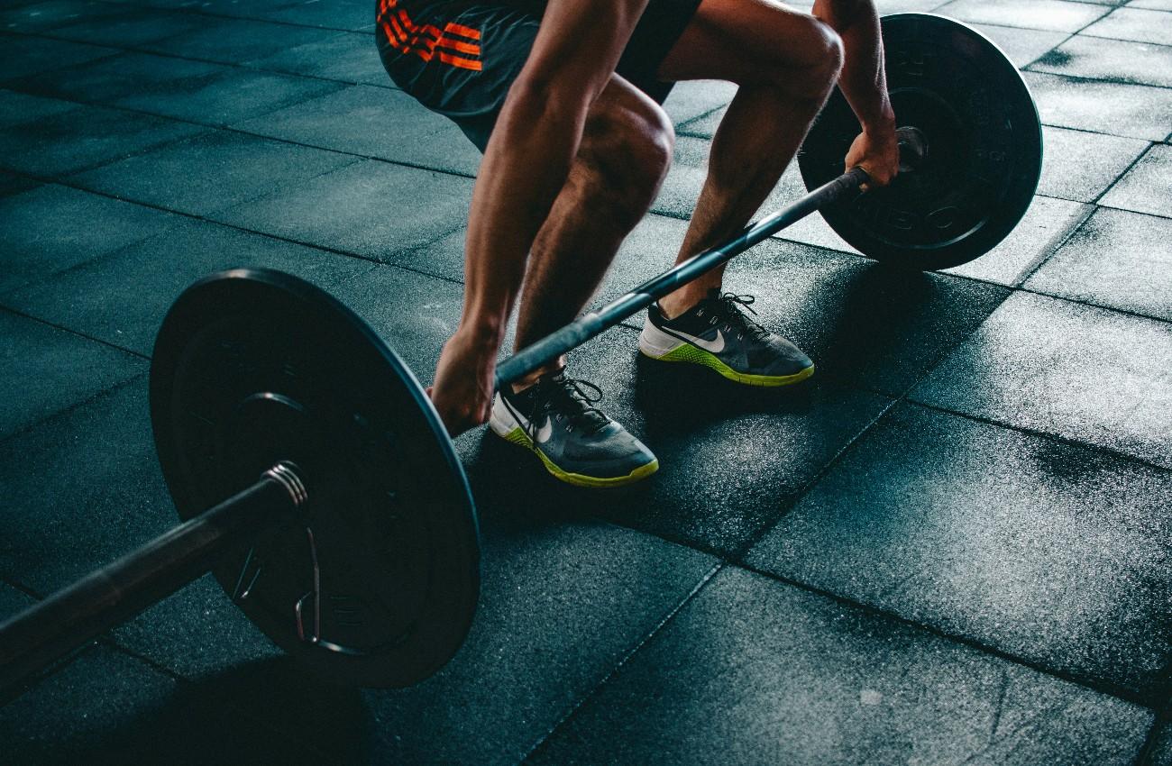 Person crouching to lift a weighted barbell from a rubber gym floor.